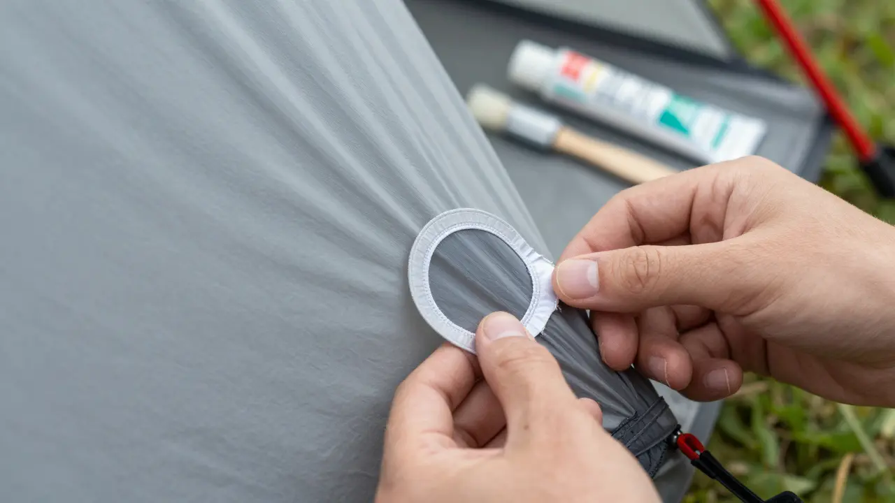 Detail ruky aplikující kulatou nylonovou záplatu na trhlinu v plátně stanu.